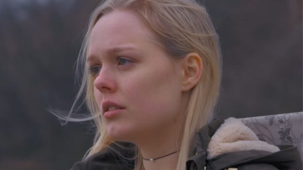 a blonde girl with a worried face wearing a winter jacket